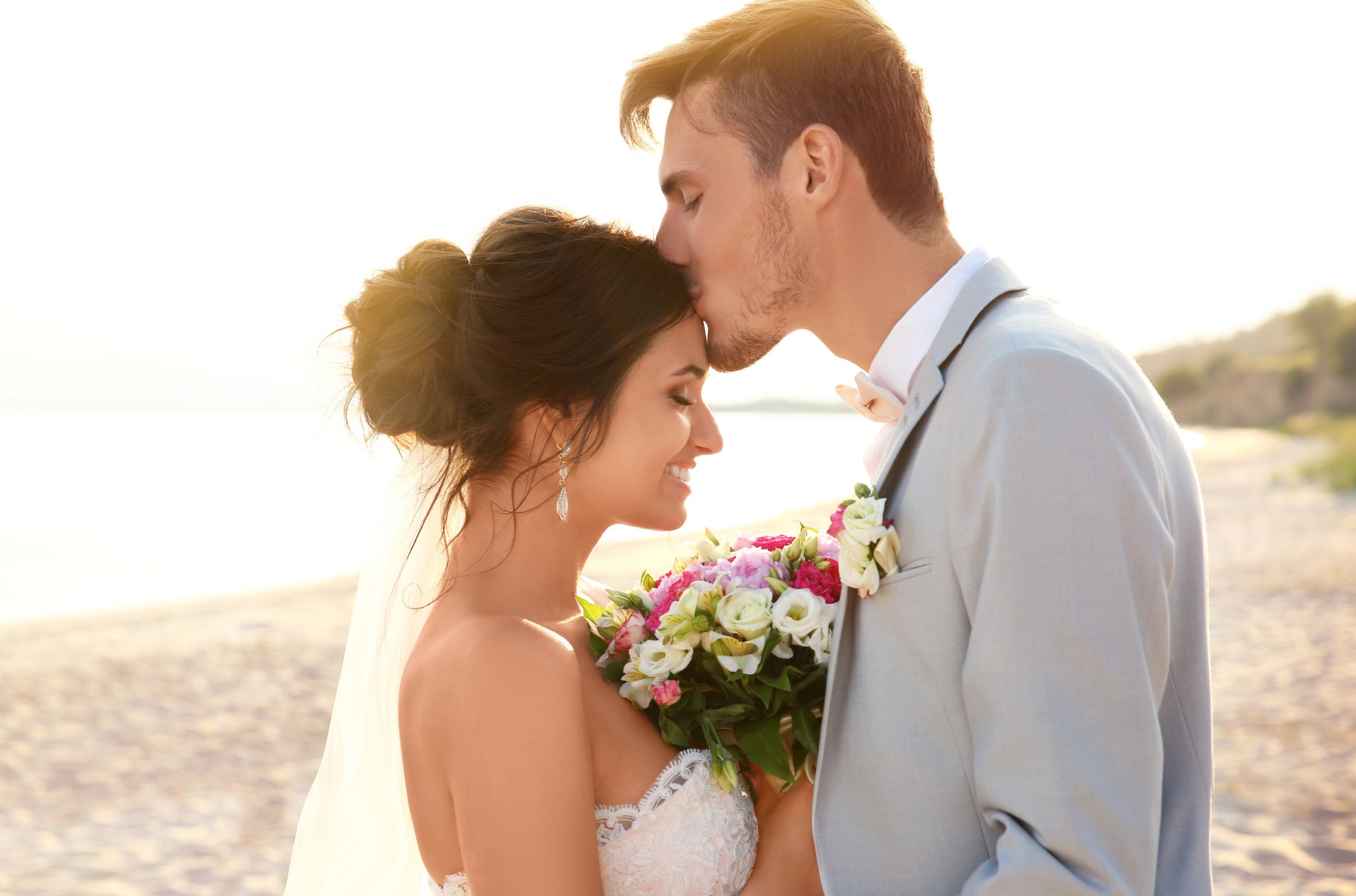 Novio besando la frente de la novia en la playa al atardecer